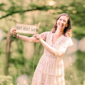 Damaris Hoppler in geblümtem Kleid hält Schild mit Aufschrift 'WISH IT, DREAM IT, DO IT!', lächelt in die Kamera