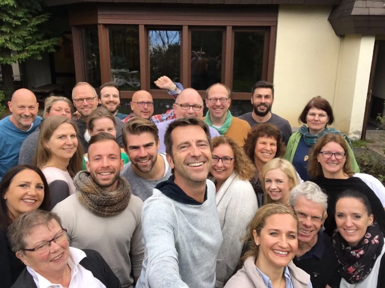 Gruppenfoto von etwa 25 Personen vor einem Gebäude mit großen Fenstern, lächelnd und eng beieinander stehend