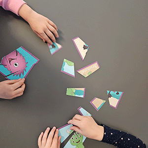 Kinder spielen Monsterschnitzeljagd mit ausgeschnittenen Monsterkarten auf grauem Untergrund