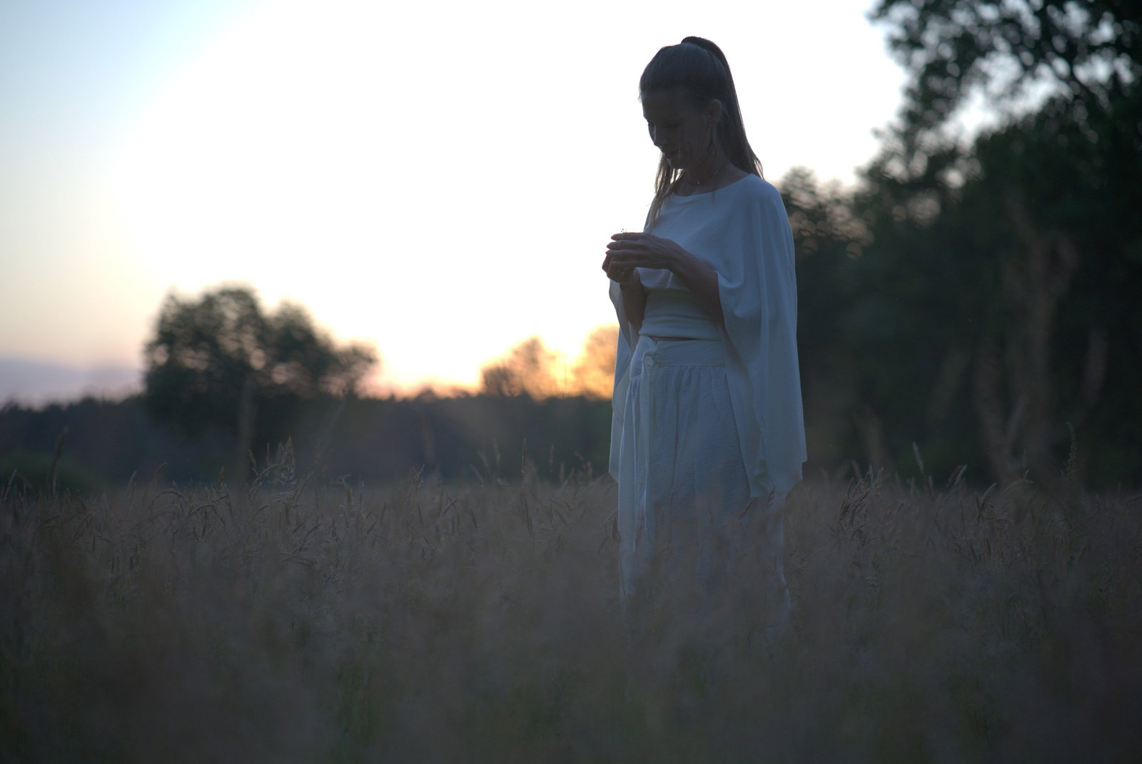 Frau in weißem Gewand auf Feld bei Sonnenuntergang in nachdenklicher Pose