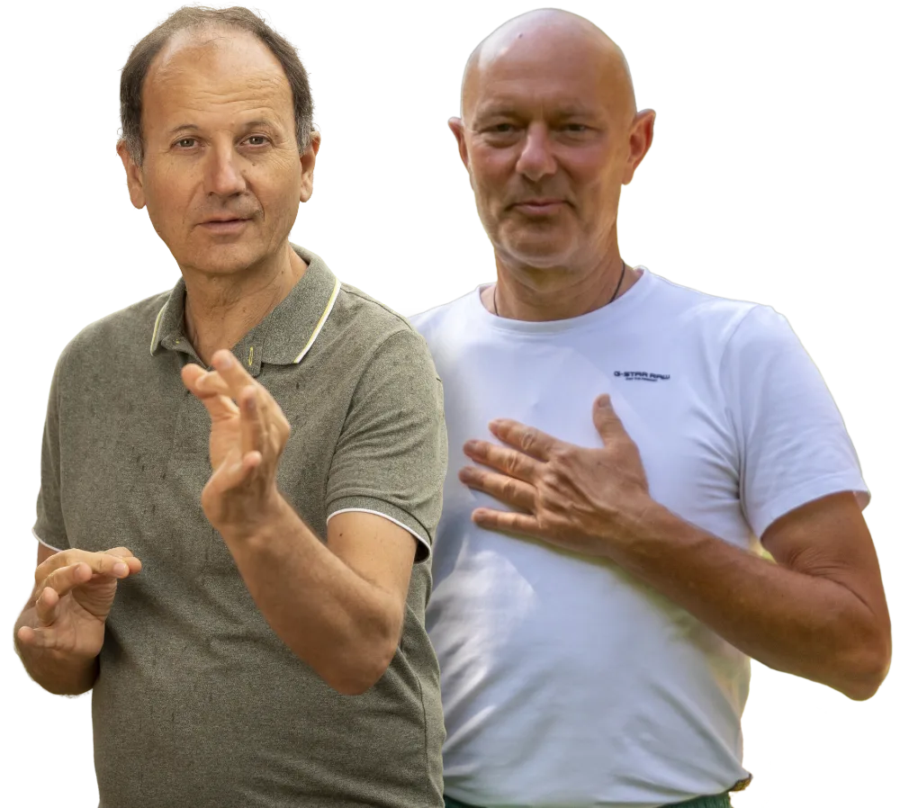 Zwei Männer mittleren Alters nebeneinander gestikulierend, einer in beigem Poloshirt, einer in hellblauem T-Shirt