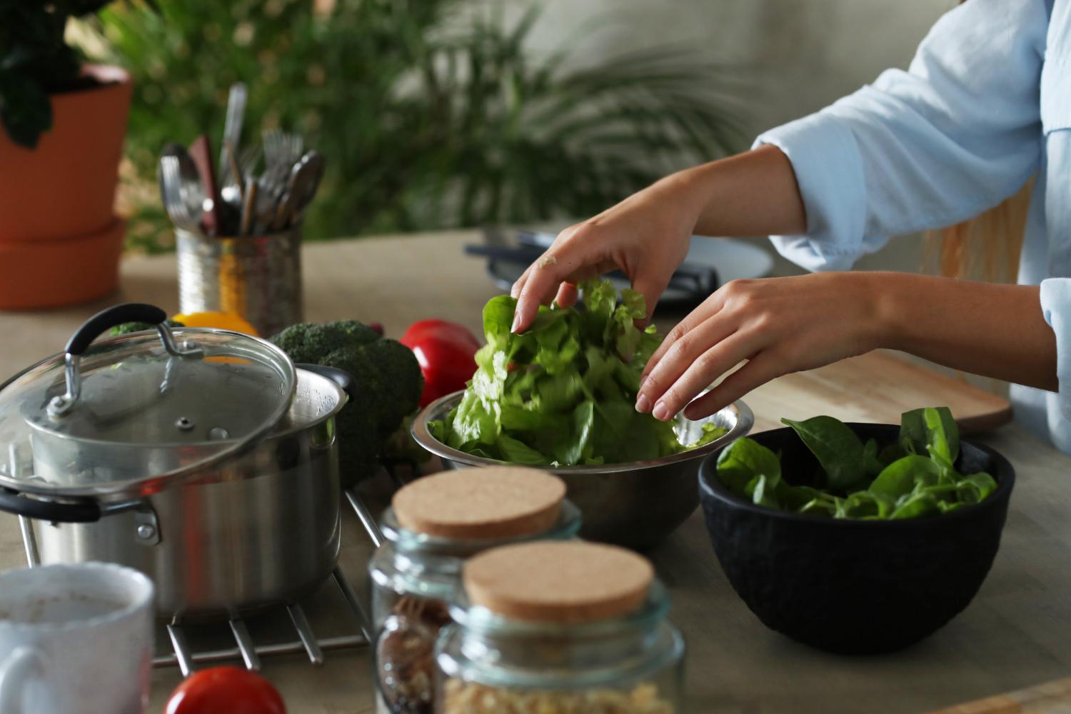 Ayurveda-Kochkurs – Videokurs für gesunde Ernährung 2 Frau in hellblauem Hemd bereitet frisches Gemüse zu, schneidet Salat in einer Schüssel, Kochutensilien und Pflanzen im Hinter