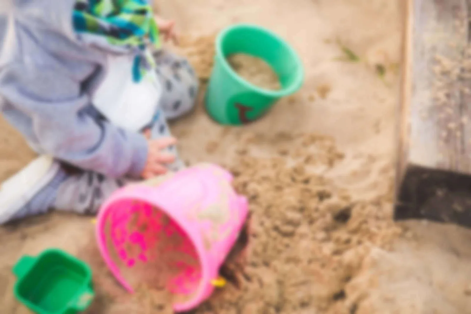 Kleinkind spielt mit bunten Schaufeln und Eimern im Sand