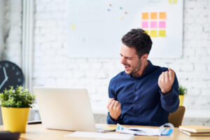 Mann im Büro vor Laptop jubelt erfolgreich, moderne Arbeitsumgebung