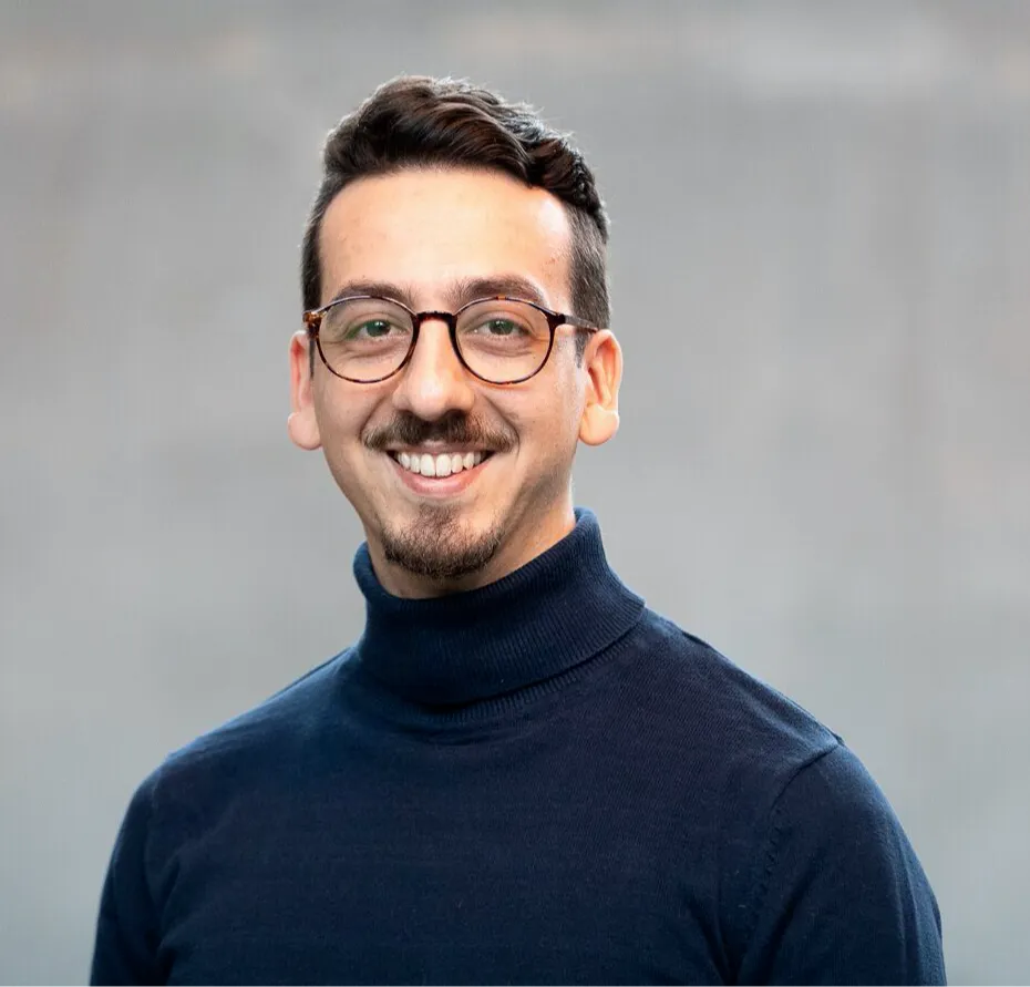 Porträt eines lächelnden Mannes mit Brille und dunklem Rollkragenpullover vor grauem Hintergrund