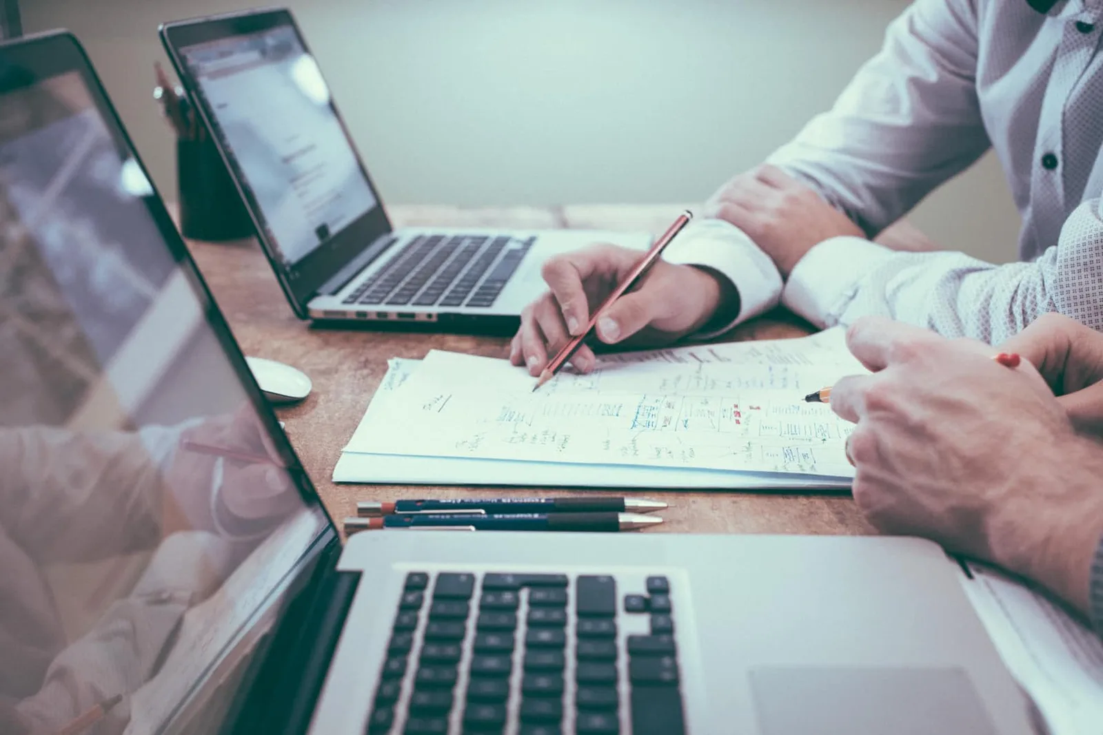 Geschäftspersonen arbeiten zusammen an Dokumenten mit mehreren Laptops am Tisch