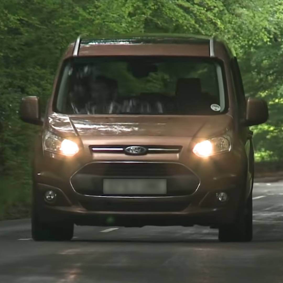 Ford Grand Tourneo Connect braun fahrend auf Waldstraße, Frontansicht mit Scheinwerfern