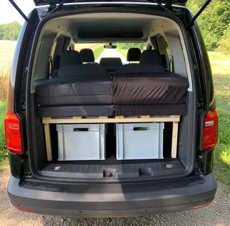 VW Caddy mit zusammengeschobenem Autobett, Matratze und weißen Aufbewahrungsboxen