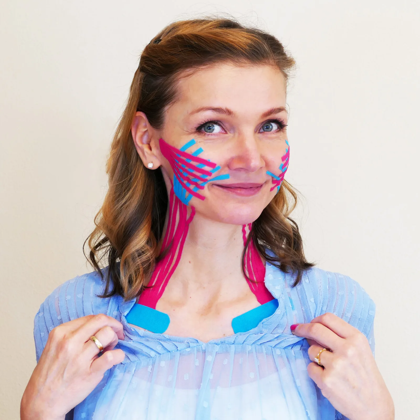 Beauty Taping – Videokurs zur Gesichtsstraffung von Christina Schmied 4 Frau mit Beauty Tape in Pink und Blau auf Wangen und Gesicht, demonstriert die Tapingtechnik