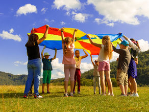 Gruppe von Kindern hält bunten Regenbogen-Fallschirm im Freien