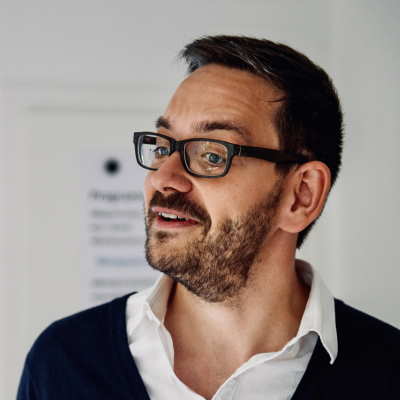 Portrait von Carsten Müller, Mann mit Brille, dunklem Hemd und weißem Kragen
