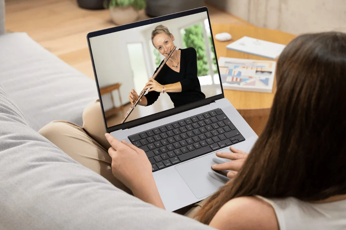 Frau mit Laptop schaut auf Bildschirm, Dozentin mit Querflöte, Live-Online-Unterricht Szenerie