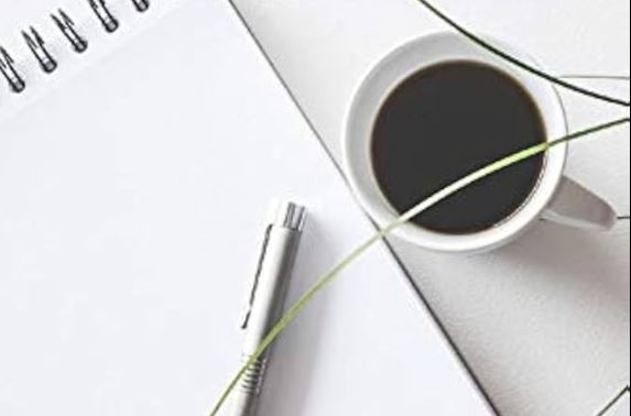 Hero-Bild Workbook mit Kaffeetasse, Notizbuch und Stift auf weißem Untergrund