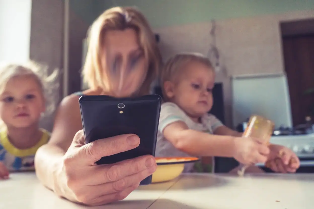 Mutter und zwei Kinder, Frau hält schwarzes Tablet nach vorne, Kinder schauen auf Bildschirm, unscharfer Hintergrund
