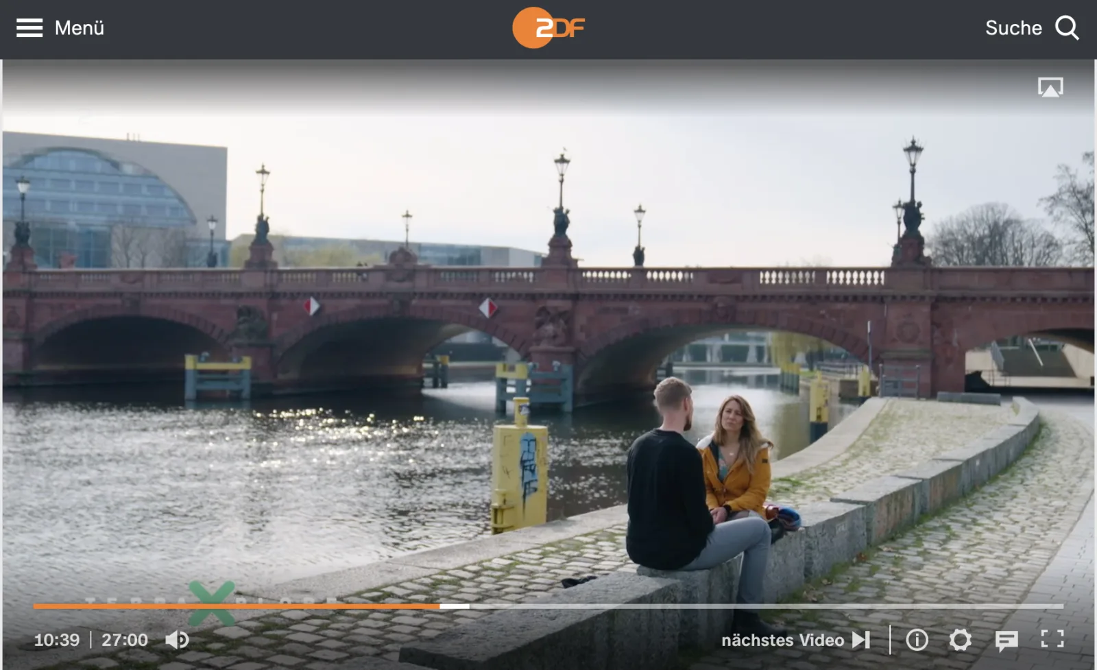 ZDF Mediathek Screenshot: Thomas und Frau sitzen sich an roter Brücke über Fluss gegenüber, Gebäude im Hintergrund