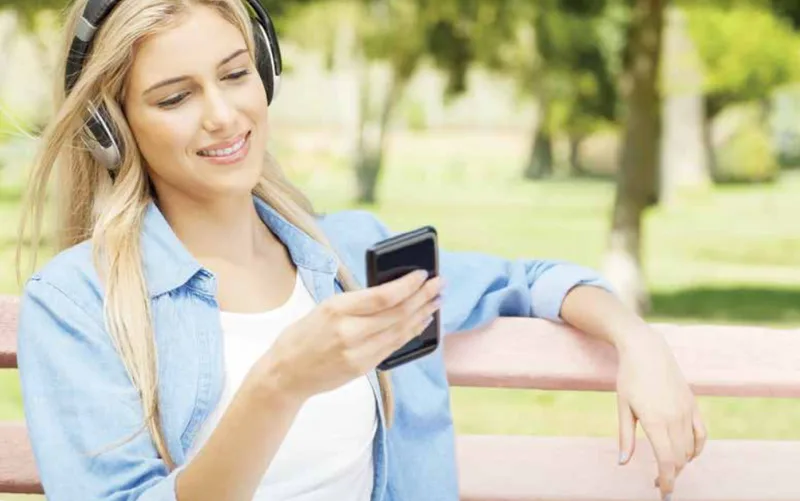 Frau mit Kopfhörern hört Audio-Programm auf Smartphone im Park