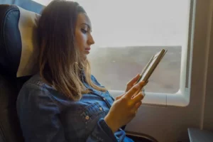 Frau im Flugzeug liest auf Tablet am Fenster, Audio-Kurs Download