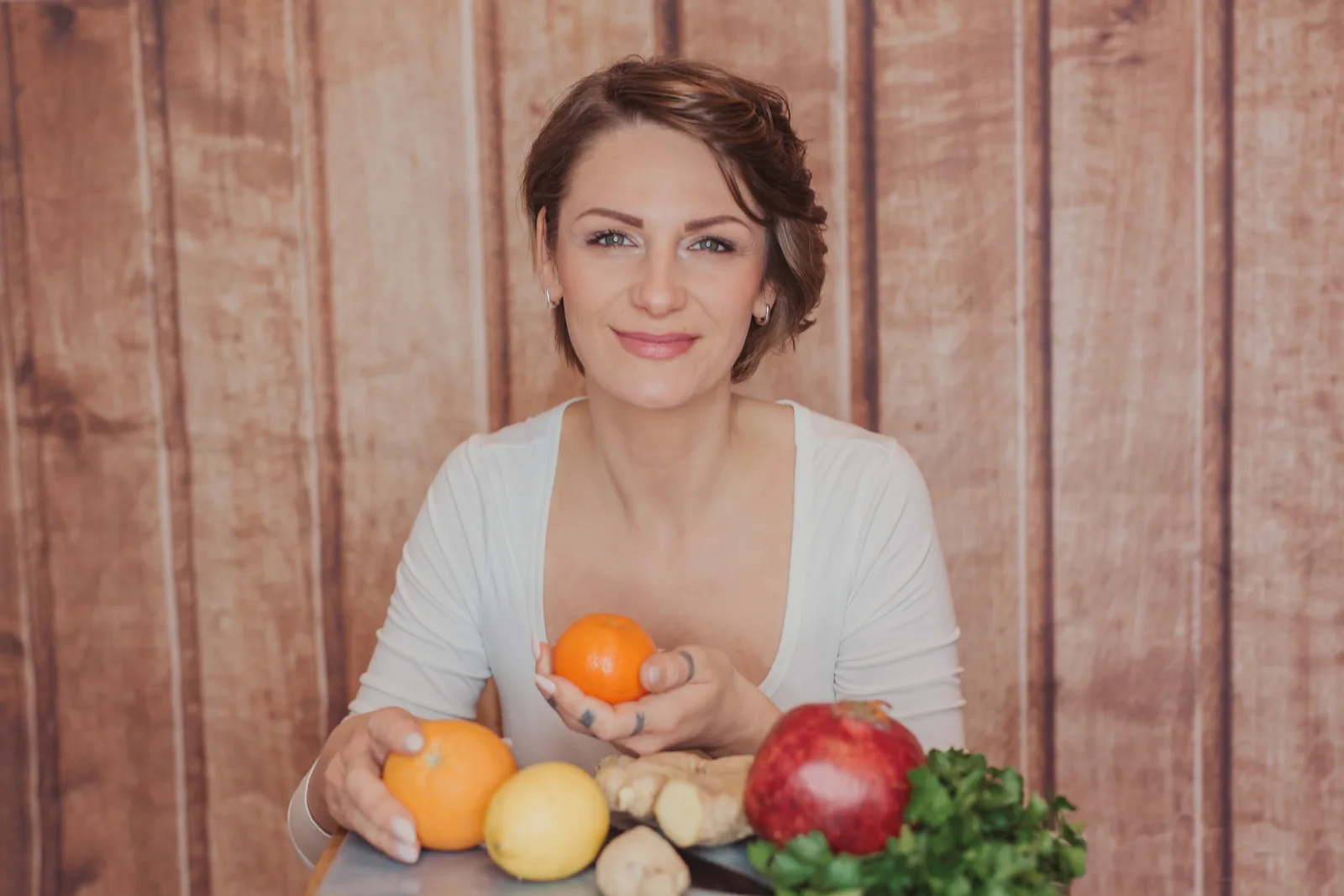 Frau mit braunem Haar in weißem Shirt hält Orangen und Apfel, gesunde Lebensmittel auf Tisch, Body Balance Hormonbasiertes Ab
