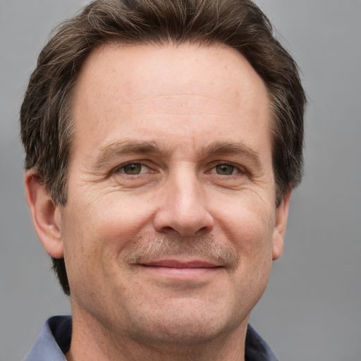 Porträt eines Mannes mittleren Alters mit braunem Haar gegen grauem Hintergrund