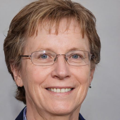 Porträt einer älteren Frau mit braunem Haar und Brille, lächelnd