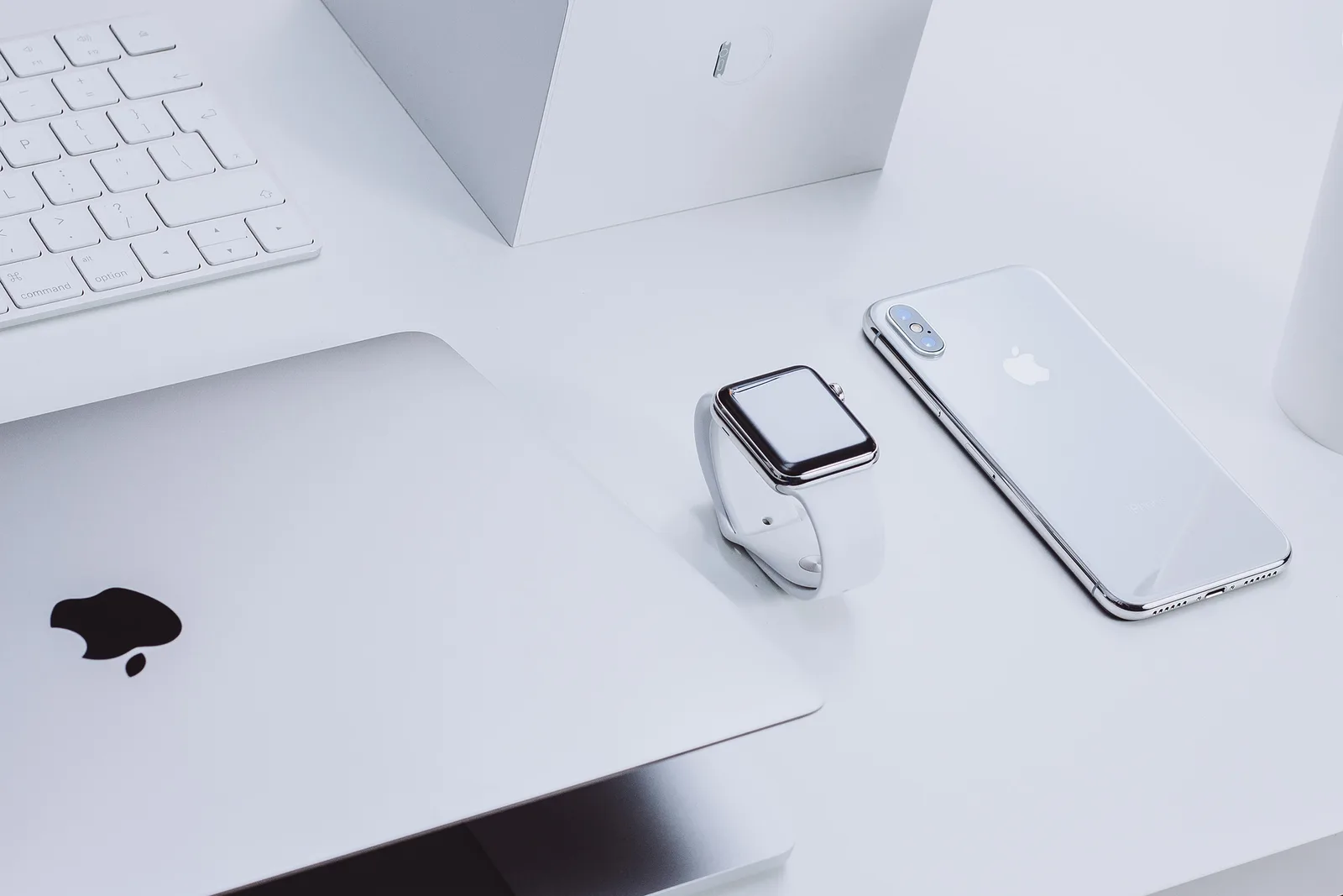 Workspace mit weißem Keyboard, Laptop, Smartwatch, iPhone und Apple-Logo-Mousepad auf weißer Oberfläche