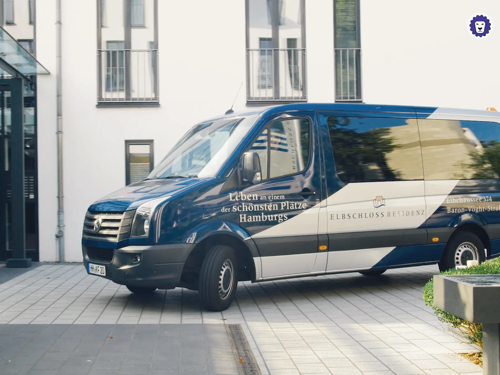 Blauer und beiger VW-Transporter mit Elbschloss-Residenz-Beschriftung vor modernem Wohnhaus