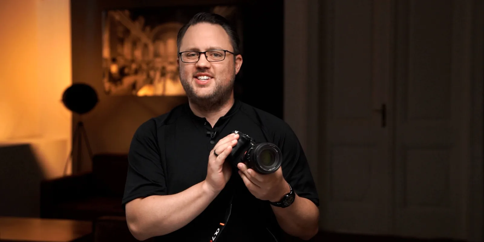 Patrick Schörg präsentiert Boudoir Secrets Masterclass mit Kamera vor orangem Studiolichthintergrund