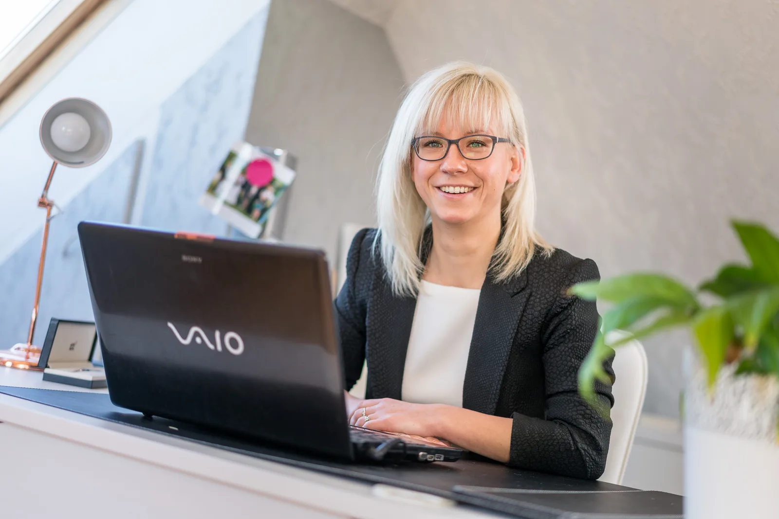 BQ-Club Adventskalender VIP – Videokurs für Online-Business 3 Frau mit weißem Haar und schwarzem Blazer arbeitet an Laptop am weißen Schreibtisch, grüne Pflanze im Hintergrund