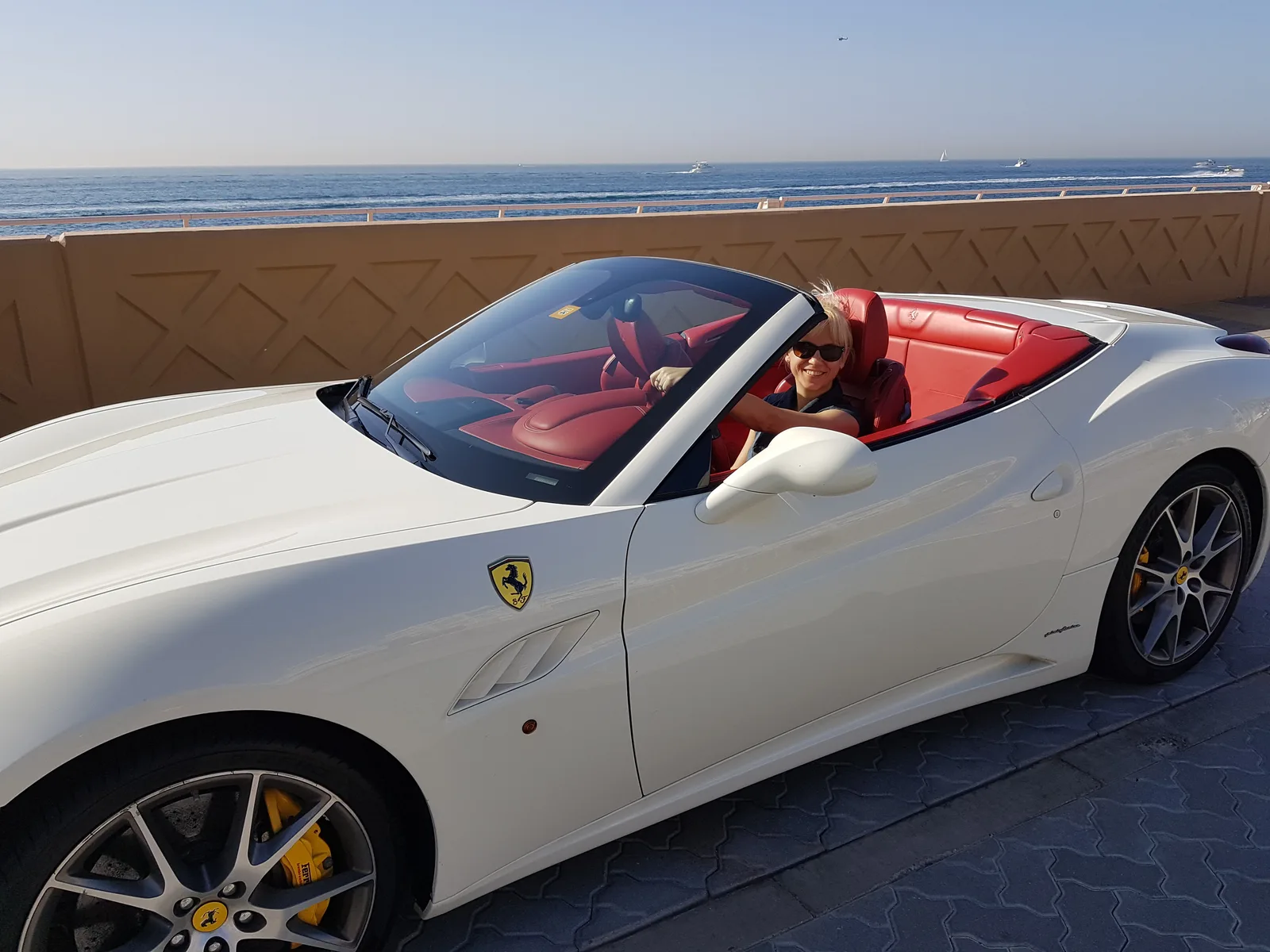 BQ-Club Adventskalender VIP – Videokurs für Online-Business 1 Frau mit weißem Haar und rotem Tuch sitzt in weißem Ferrari Cabrio vor Meereshorizont