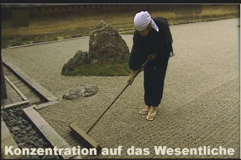 Frau in schwarzem Anzug mit weißem Kopftuch harkt konzentriert Kiesfläche in japanischem Garten