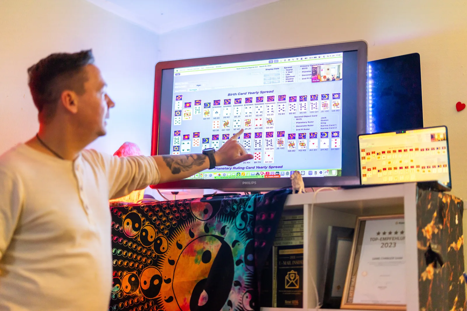 Mann zeigt auf Computerbildschirm mit Geburtshoroskop-Spreadsheet und Tarot-Kartenanalyse