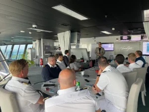 Workshop-Szenario mit Teilnehmern an großem Tisch auf Schiff, Moderator präsentiert
