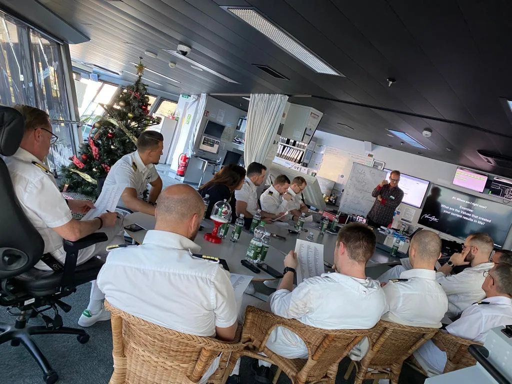 Online Business Workshop in Büroraum mit Teilnehmern an Tischen, Weihnachtsdeko sichtbar