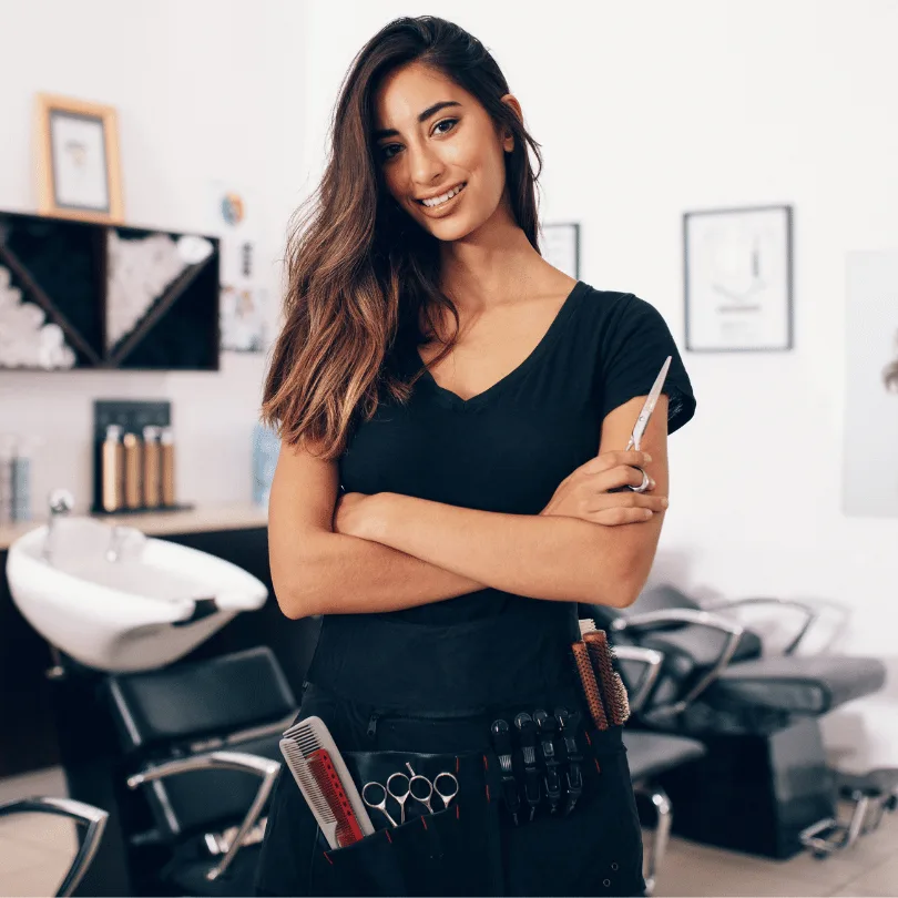 Junge Friseurin mit dunklen Haaren in schwarzem Shirt mit Schere in Friseursalon