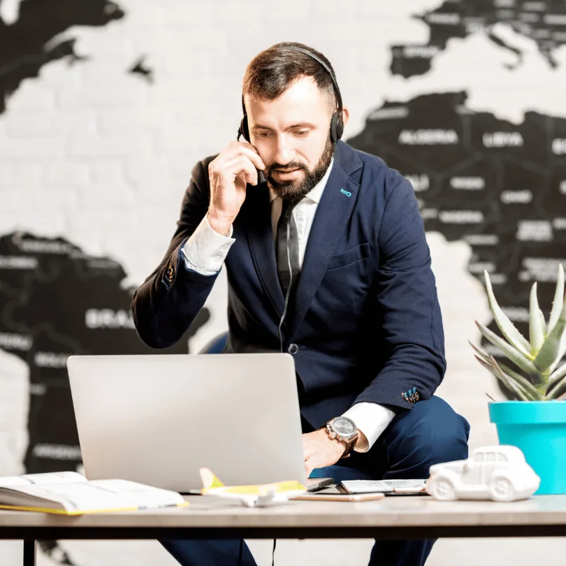 Geschäftsmann mit Headset am Laptop-Schreibtisch, vor Weltkarte, professionelle Business-Umgebung