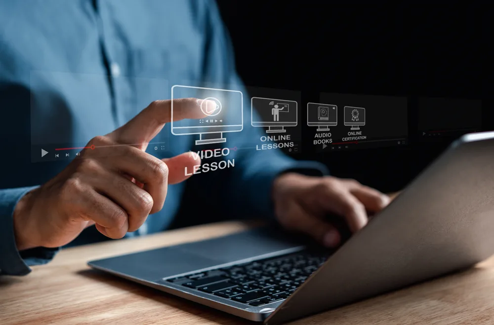 Hände halten transparentes Tablet mit Video-Lesson Icon, Laptop im Hintergrund, E-Learning Symbole für Online Lessons, Audio
