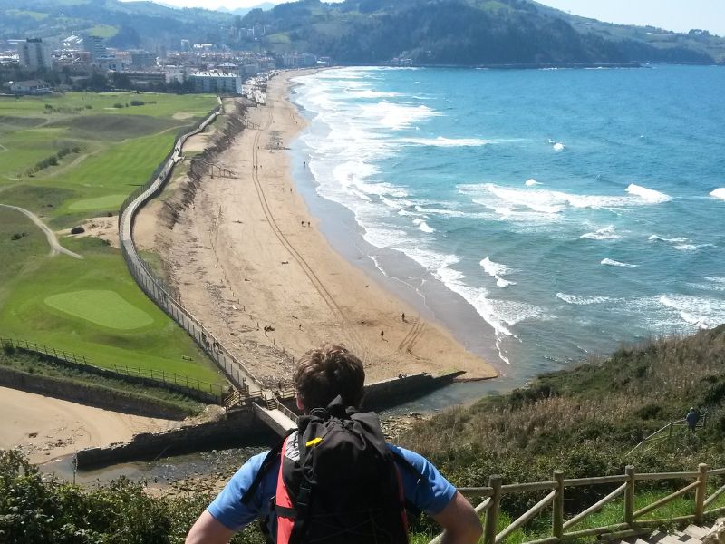 Herrlicher Strandabschnitt des Camino del Norte bei Zarautz mit Wellen und grünen Wiesen