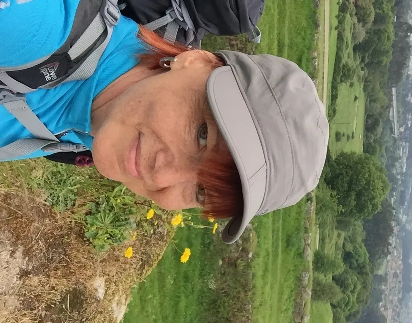 Frau mit Rucksack und Kappe auf Wanderweg, leicht nach rechts geneigt