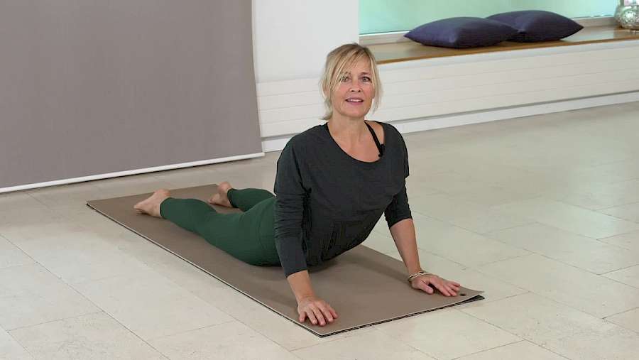 Frau in schwarzem Langarmshirt und grüner Yogahose in Liegestützposition auf Yogamatte in hellem Studio