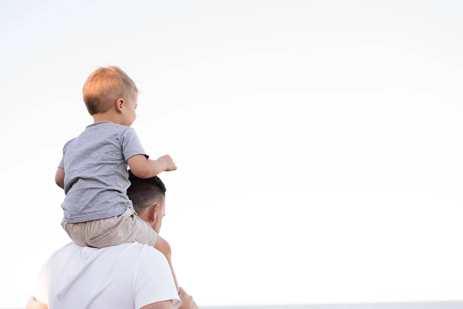 Kleines Kind mit blondem Haar sitzt auf Schultern eines Mannes, beide schauen nach rechts