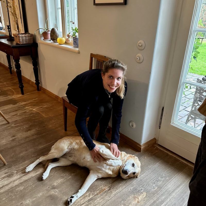 CEO Growth Mentoring – Coaching zur Unternehmensskalierung 5 Frau in schwarzem Blazer streichelt freundlich einen großen Hund in modernem Wohnzimmer