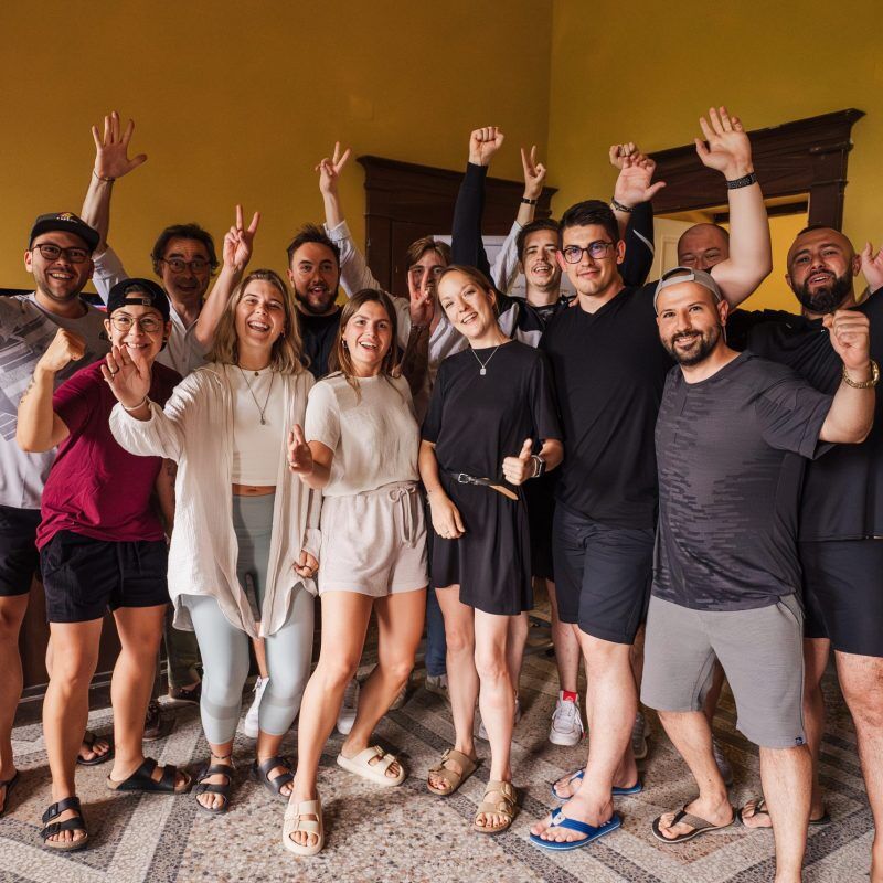 CEO Growth Mentoring – Coaching zur Unternehmensskalierung 6 Gruppe von etwa 15 Unternehmern hebt die Arme jubelnd mit erhobenen Fäusten vor gelbem Hintergrund