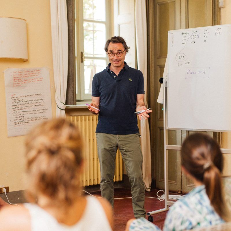 CEO Growth Mentoring – Coaching zur Unternehmensskalierung 8 Mann in dunklem Poloshirt steht vor Flipchart mit handschriftlichen Notizen und unterrichtet Gruppe