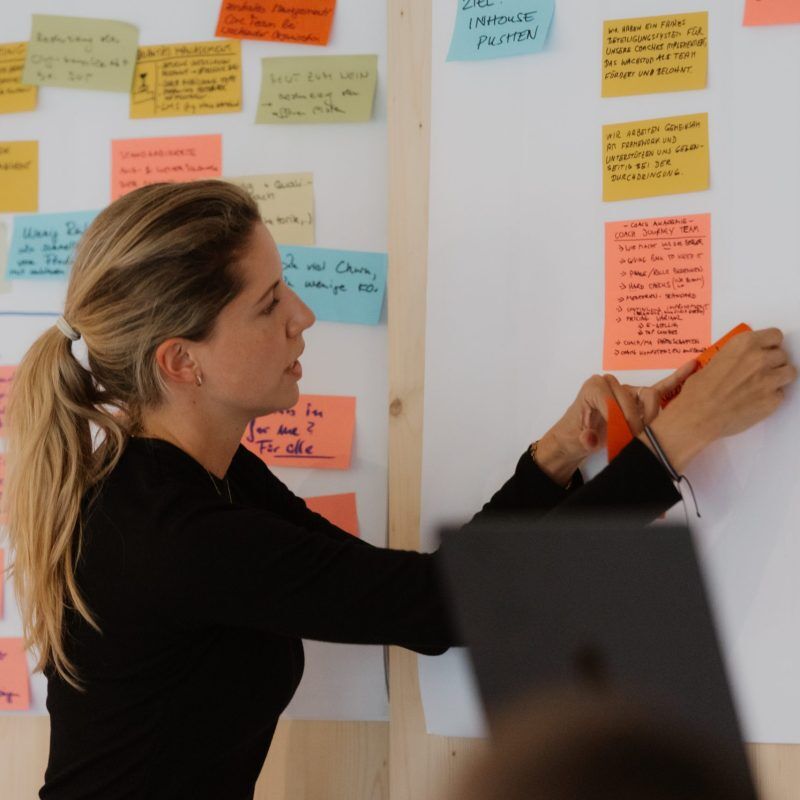 CEO Growth Mentoring – Coaching zur Unternehmensskalierung 9 Frau platziert bunte Klebezettel auf Whiteboard mit handschriftlichen Notizen und Ideen