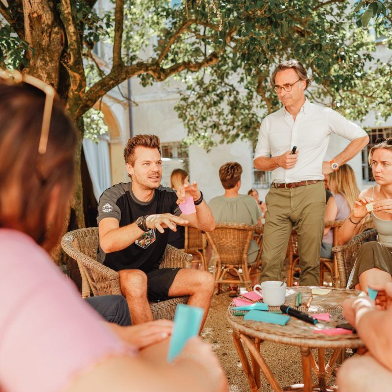 CEO Growth Mentoring – Coaching zur Unternehmensskalierung 12 Mehrere Unternehmer in entspannter Runde unter Baum diskutieren und notieren an Tischen