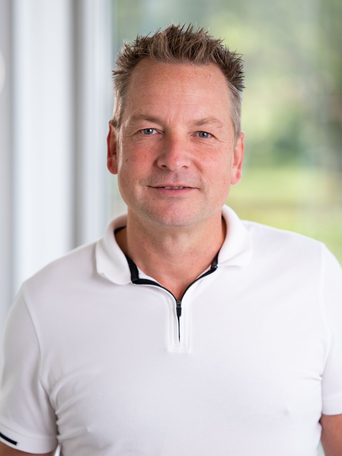 CEO Growth Mentoring – Coaching zur Unternehmensskalierung 17 Portrait von Patrick Blum, Scale Up Coach, in weißem Poloshirt vor unscharfem grünem Hintergrund