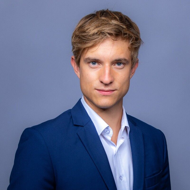 CEO Growth Mentoring – Coaching zur Unternehmensskalierung 26 Porträt von Ruben Koers, junger Mann mit Brille in dunklem Anzug vor blauem Hintergrund