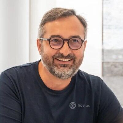 CEO Growth Mentoring – Coaching zur Unternehmensskalierung 27 Porträt von Waldemar Hanikel in dunklem Fidetus-Shirt mit Brille vor hellem Hintergrund