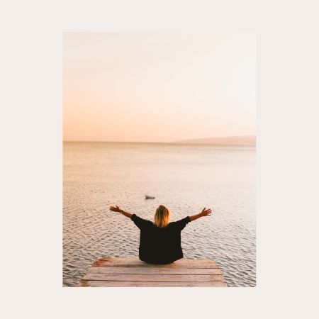 Frau beim Yoga mit ausgebreiteten Armen am Wasser bei Sonnenuntergang