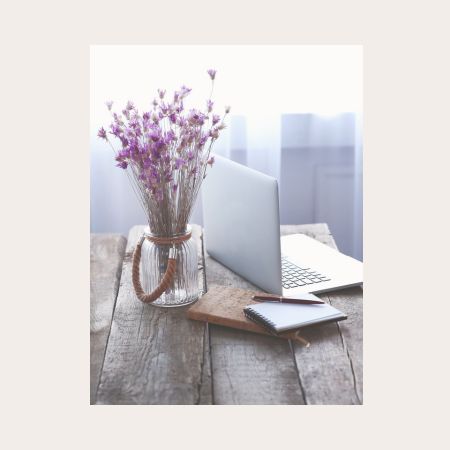 Arbeitsplatz mit lila Blumenstrauss, Laptop und Notizbuch